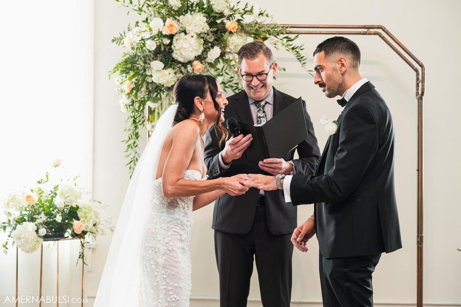 Wedding ceremony under floral arch with officiant conducting service.