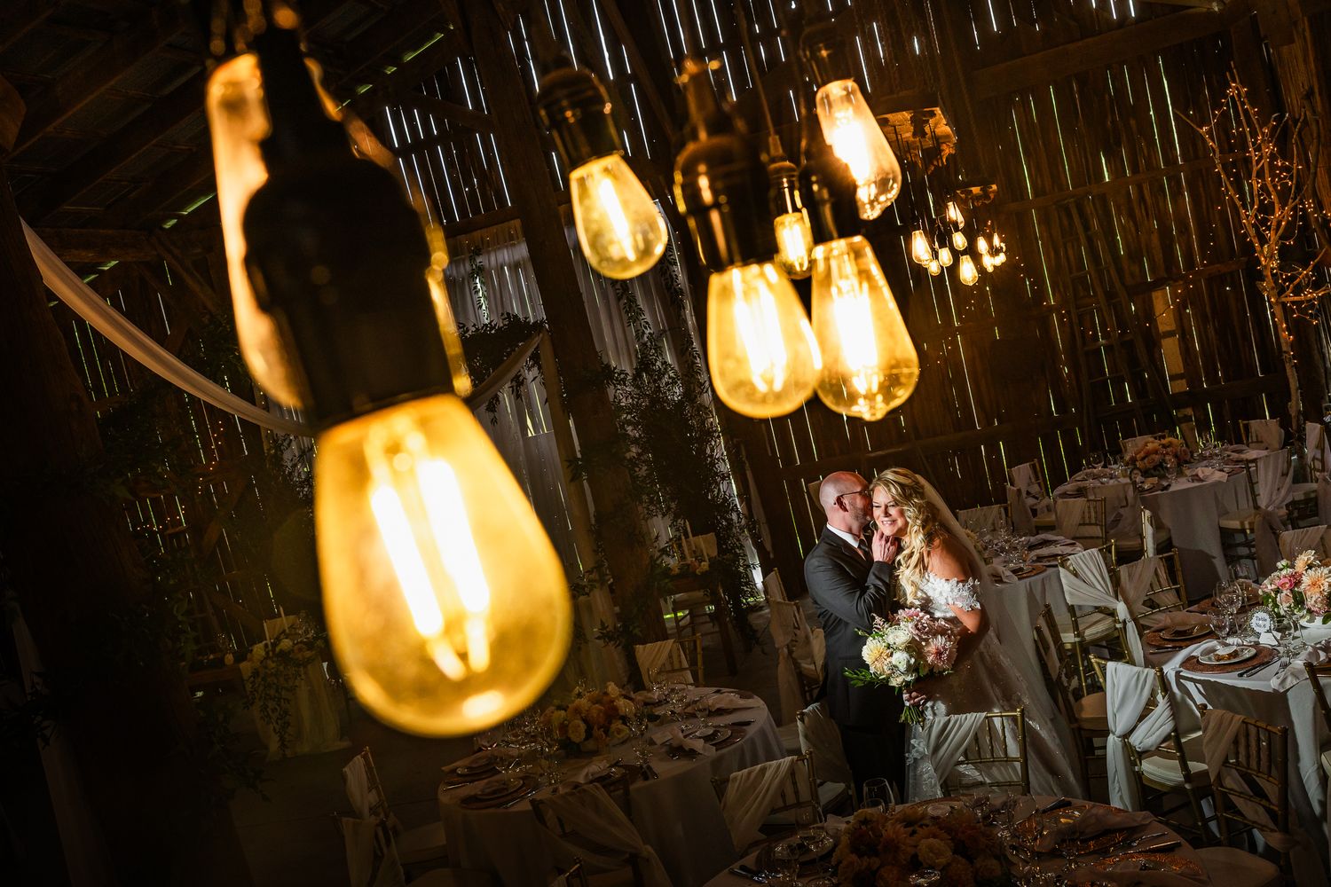 Edison bulbs hang from dark wooden beams creating moody lighting for an intimate wedding venue.