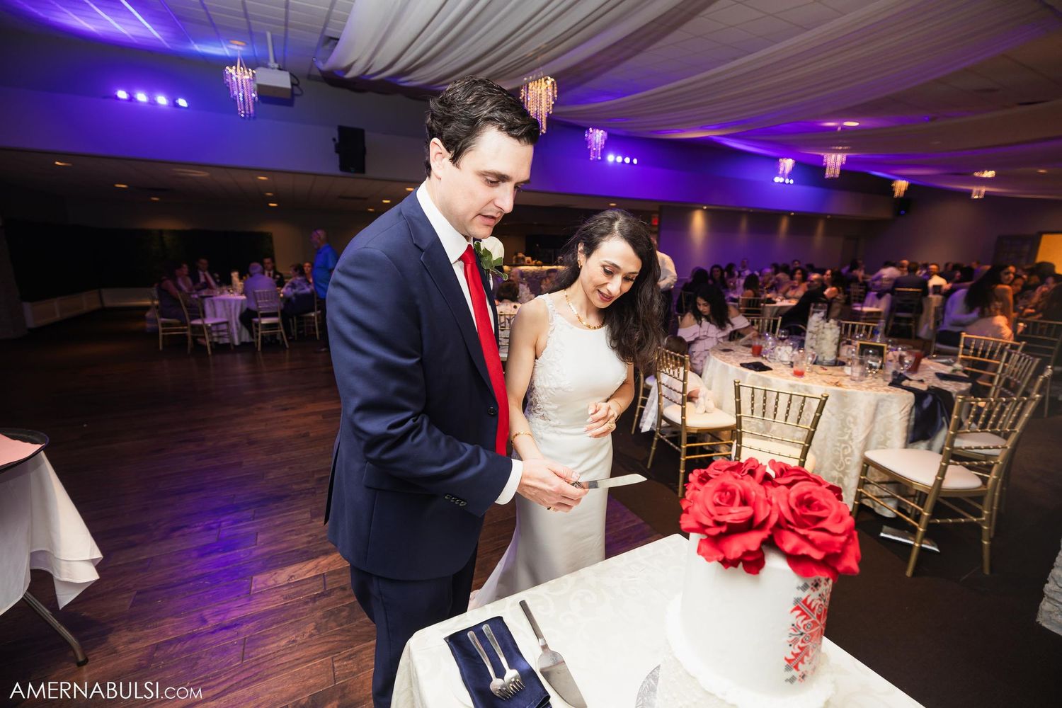 Couple cutting their wedding cake under purple ambient lighting at an elegant reception.