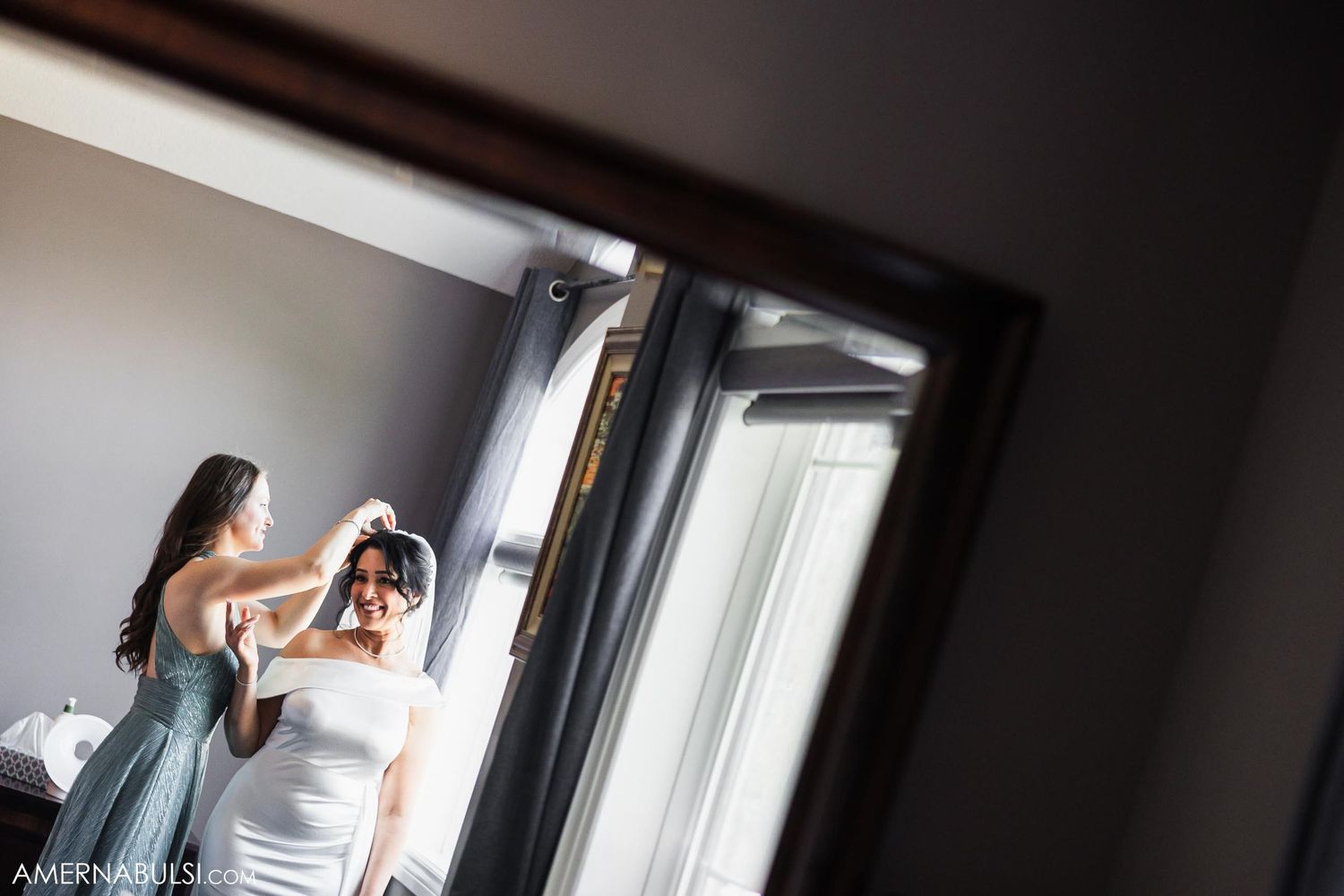 Wedding preparation scene showing bride getting final touches in mirror reflection.