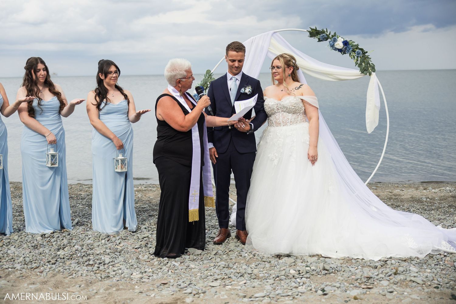 Wedding party in pastel blue dresses poses for photos by the waterfront.
