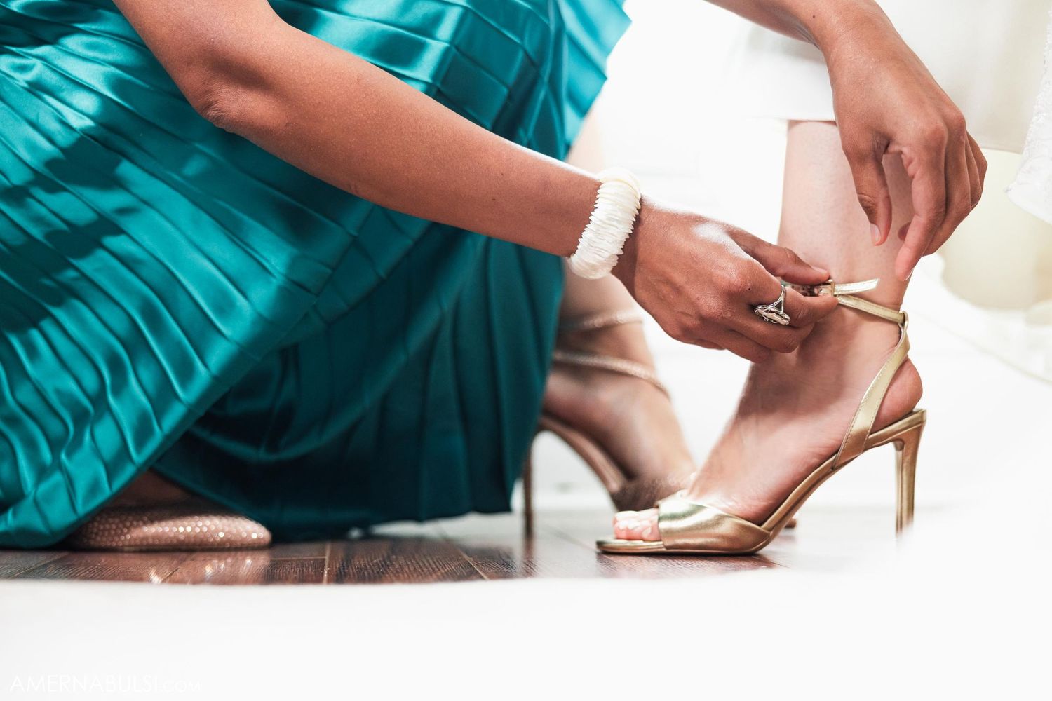 Close-up of bridesmaid adjusting gold strappy heel on wedding day.
