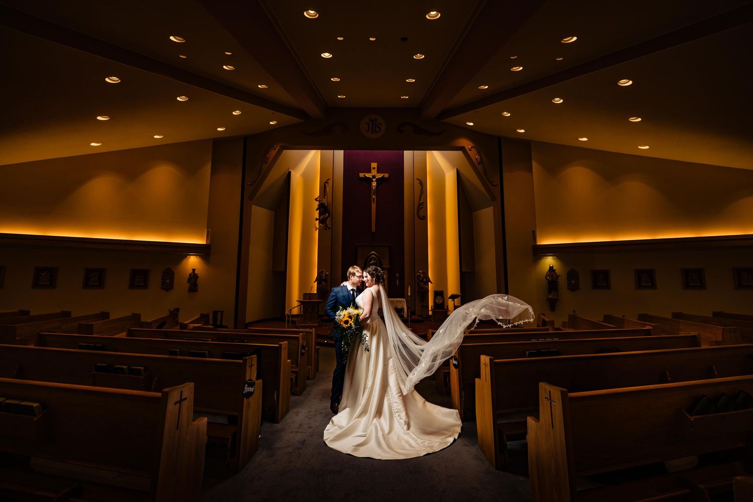 Wedding ceremony in dimly lit church with dramatic lighting and long aisle.