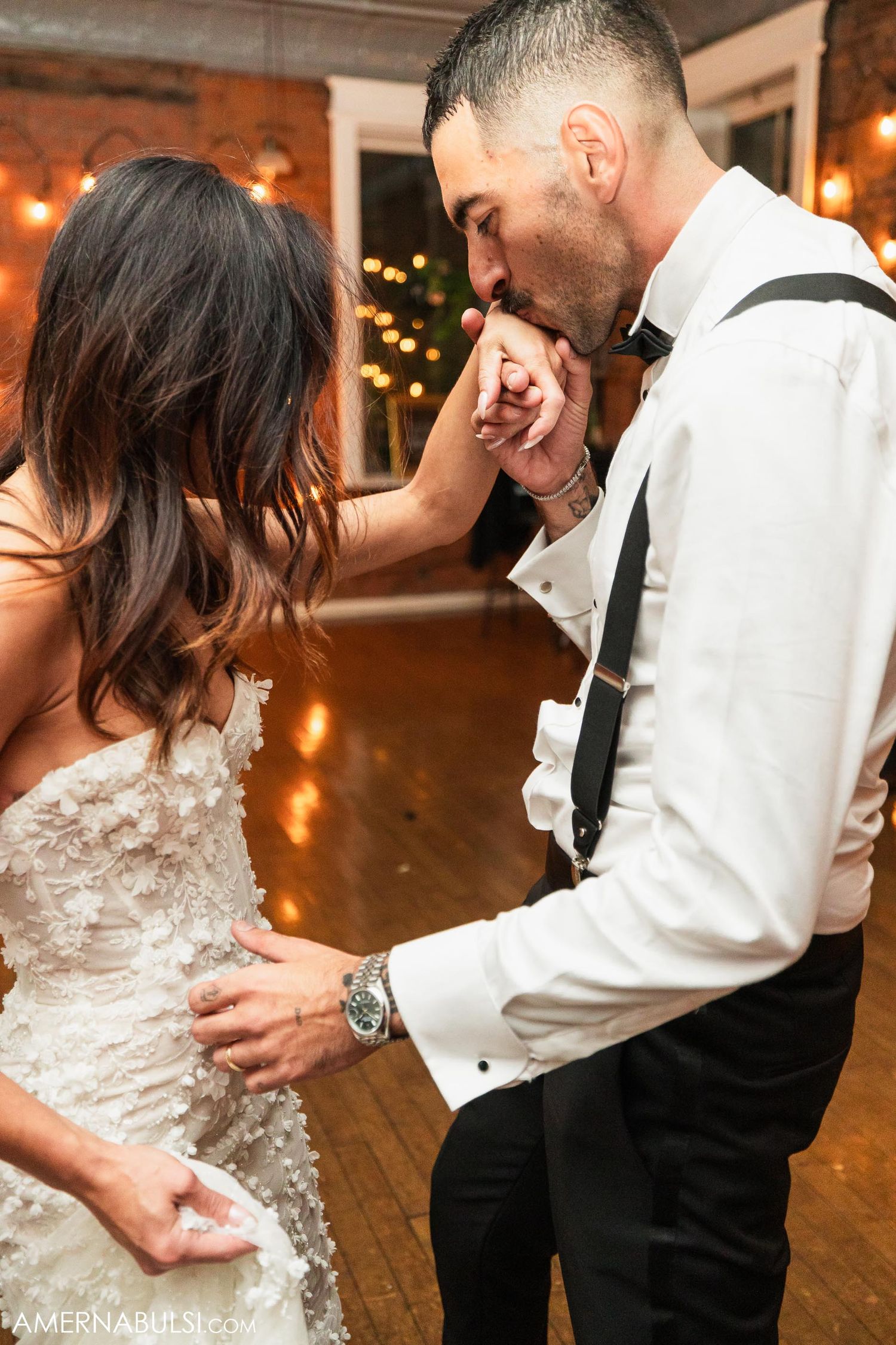 A romantic moment between newlyweds on a dance floor illuminated by string lights.