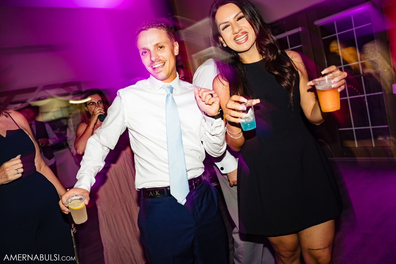 People dancing and mingling at a nightclub with purple lighting and festive atmosphere.