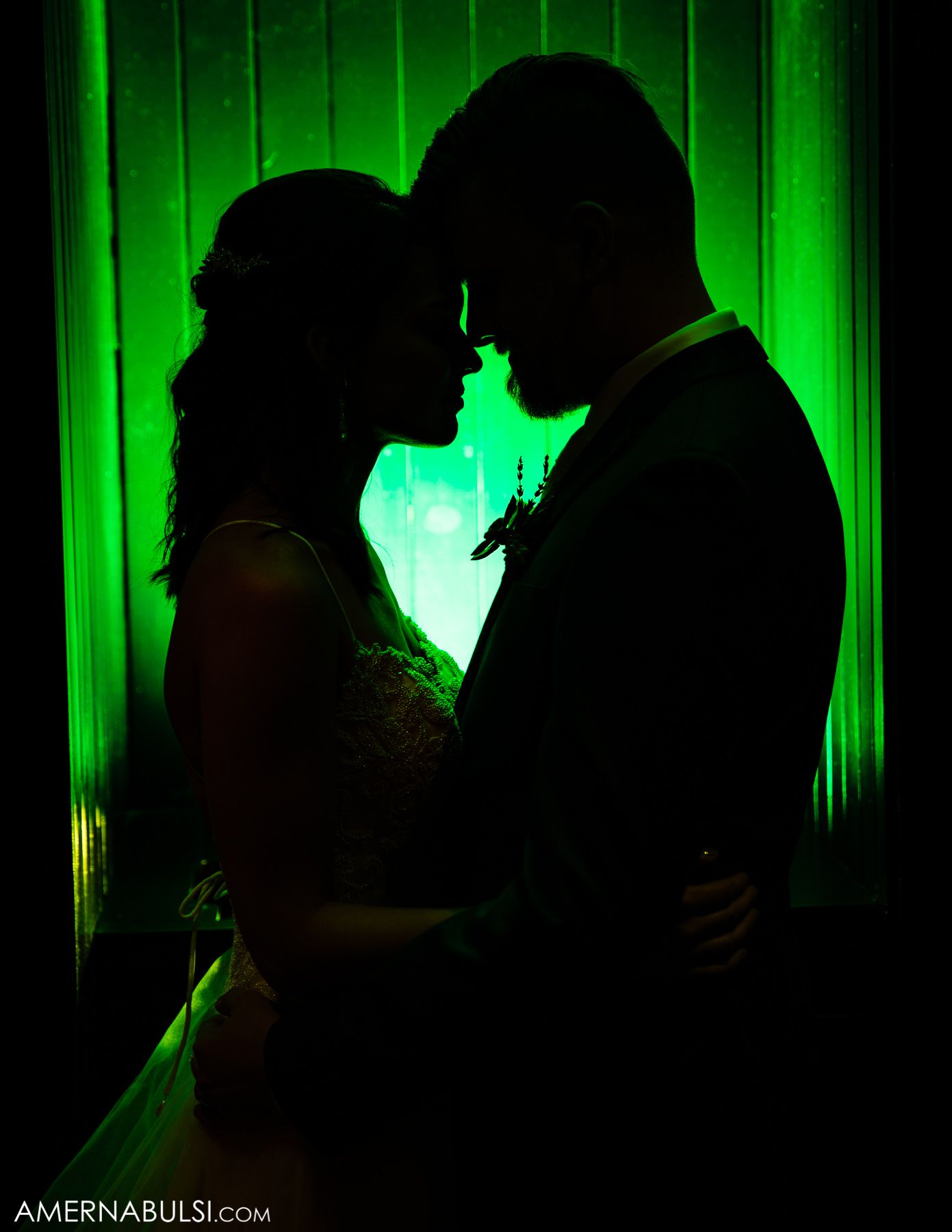 Silhouetted couple sharing an intimate moment against dramatic green lighting at a wedding reception.