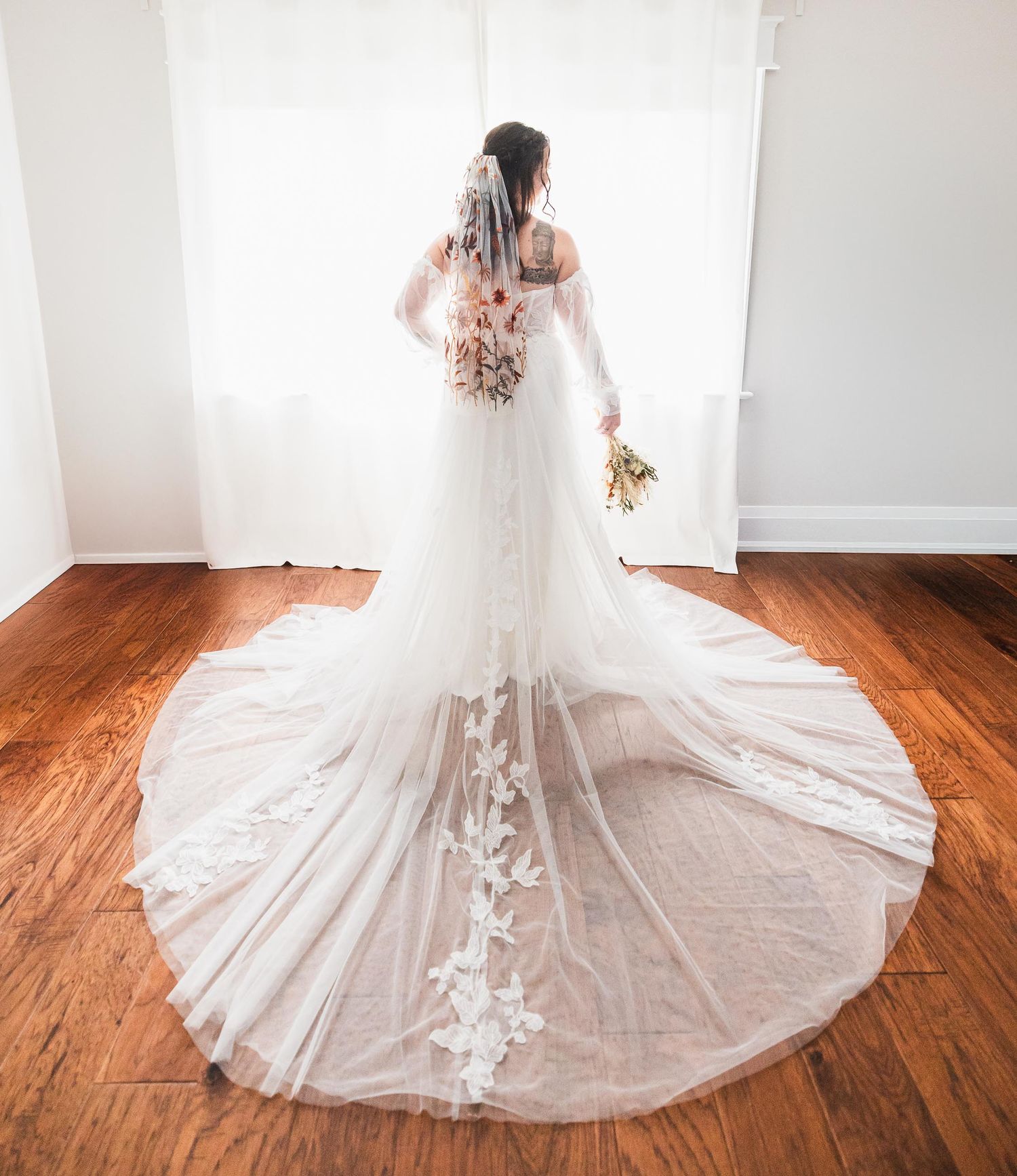 Back view of a wedding dress with intricate lace train on hardwood floors.