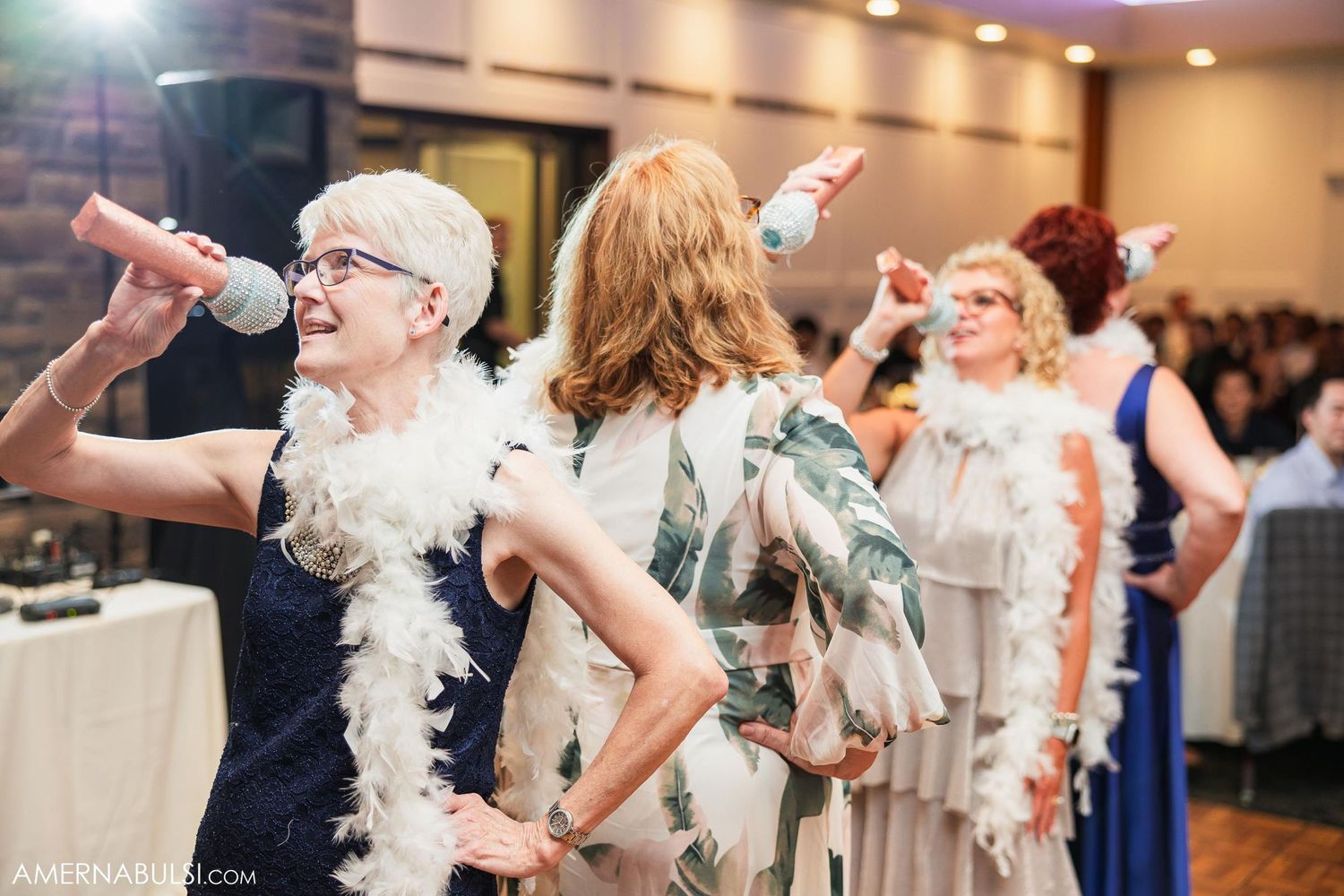 Wedding guests perform synchronized dance moves with feather boas at reception.