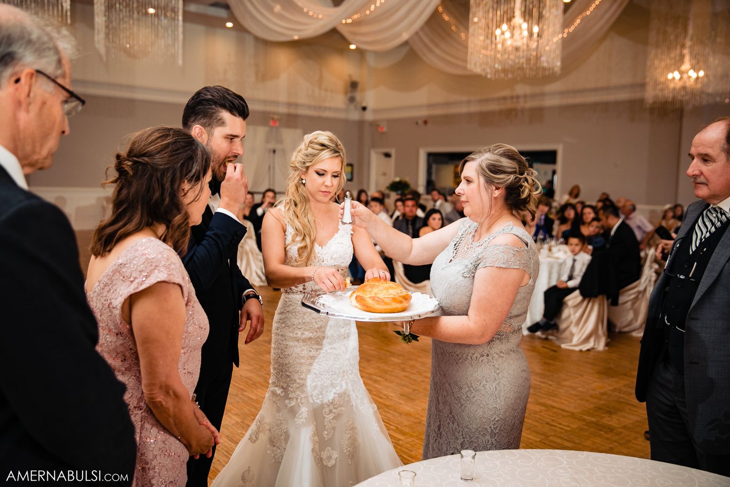 Wedding guests dance and celebrate on an elegant ballroom floor under crystal chandeliers during an evening reception.