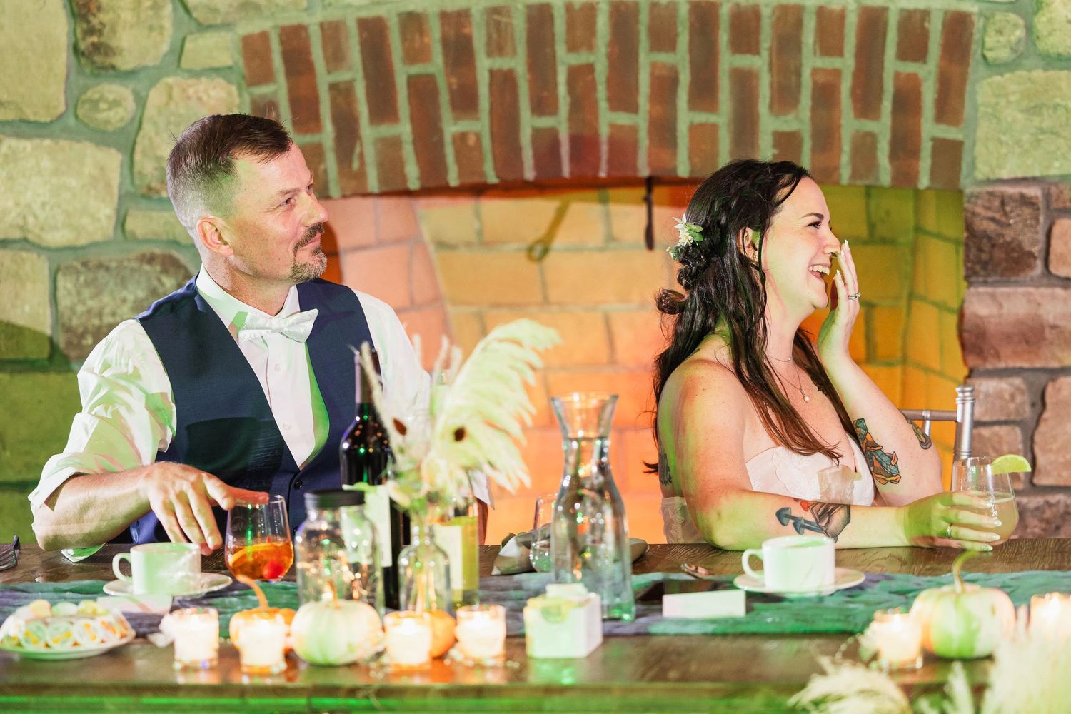 A couple shares a candid moment while seated at their reception table with drinks and decorations.