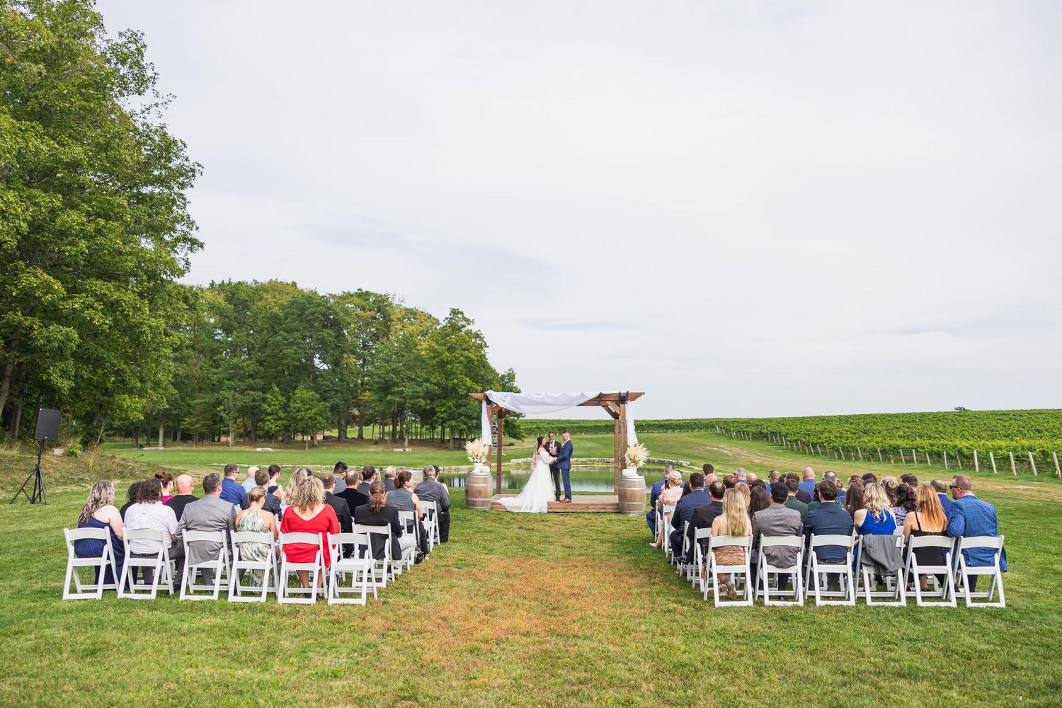 A vineyard wedding ceremony setup with white chairs and wooden arch surrounded by natural scenery.