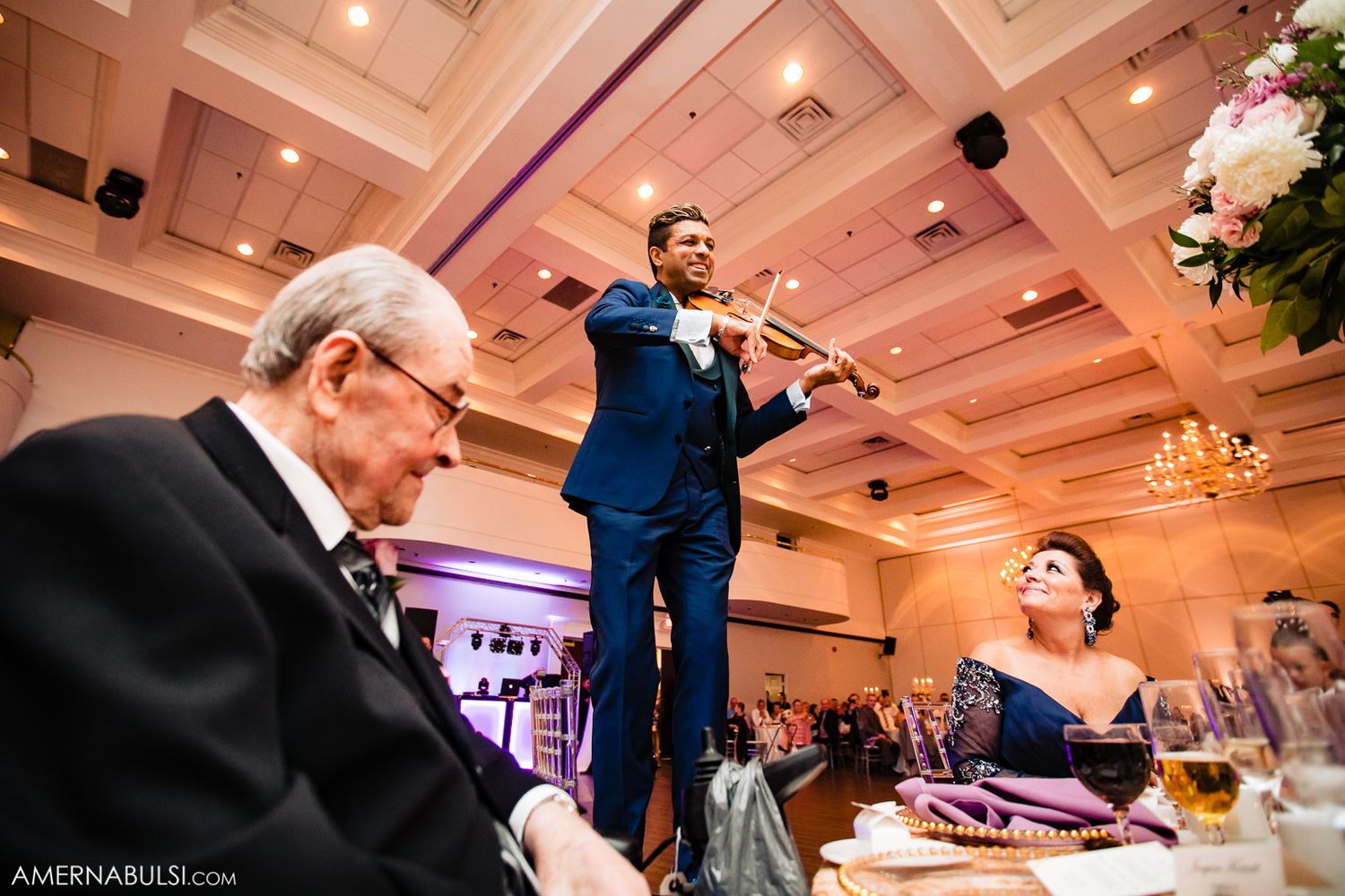 Elegant wedding reception venue with coffered ceiling, chandeliers and guests dancing in formal attire.