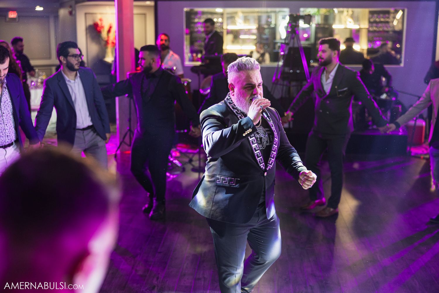 People dance together in a dimly lit room with purple lighting creating an intimate social atmosphere.