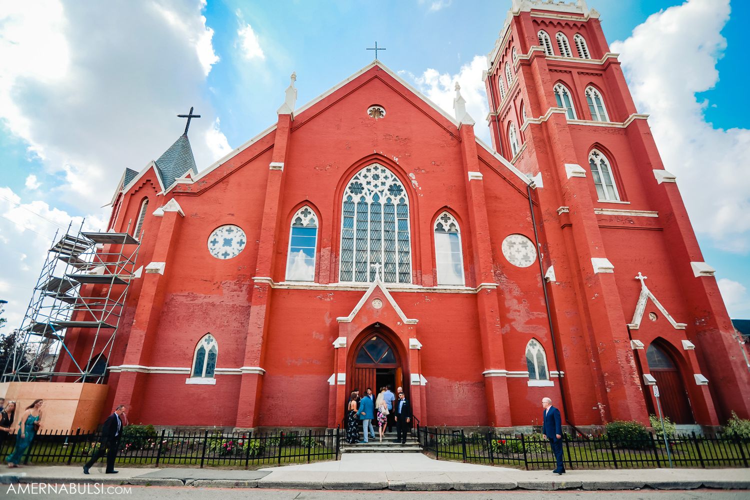 Exterior views of red brick gothic church with cross and steeple against blue sky.