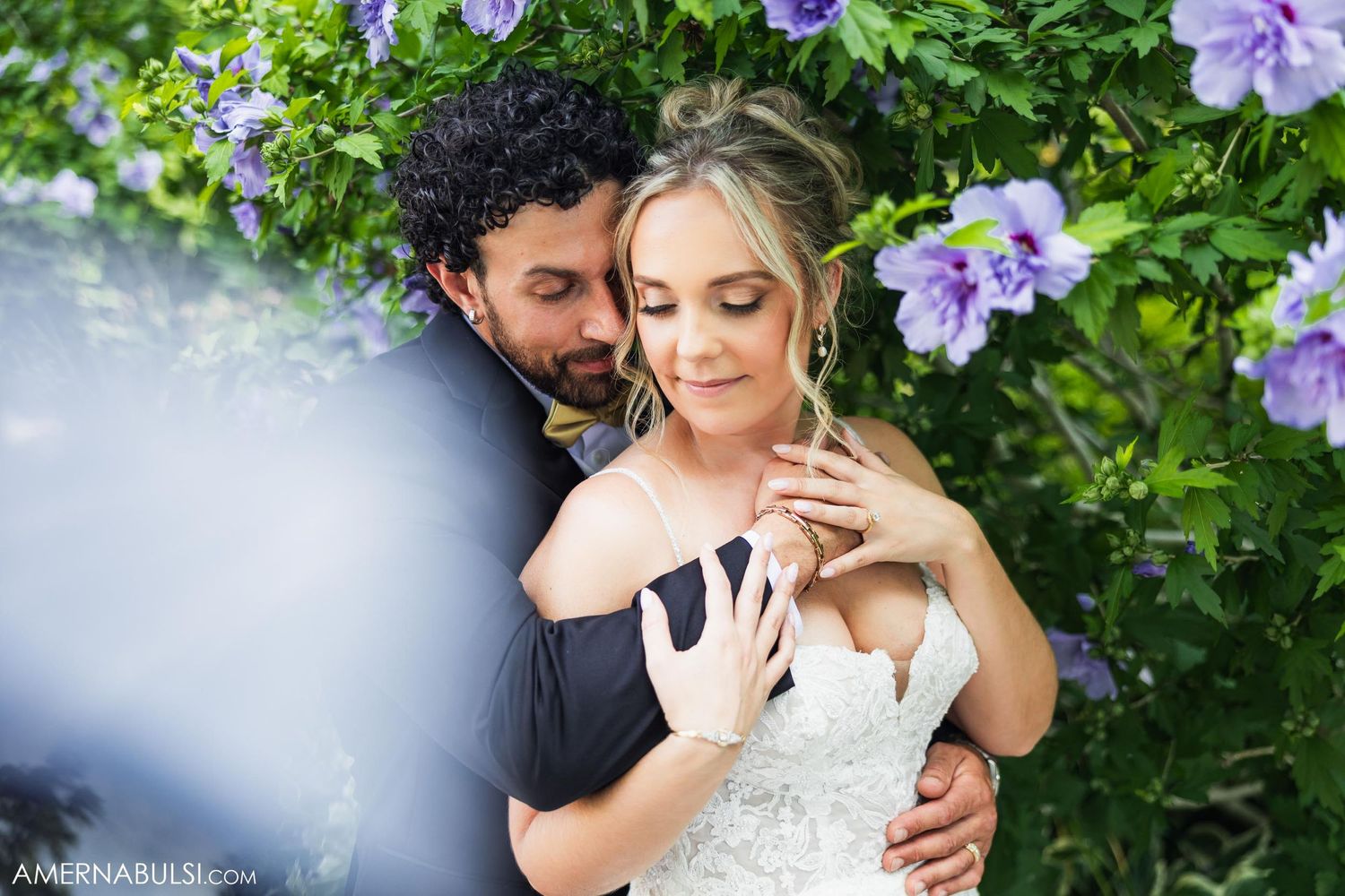 A romantic garden wedding photo with purple flowers framing a tender moment between newlyweds.