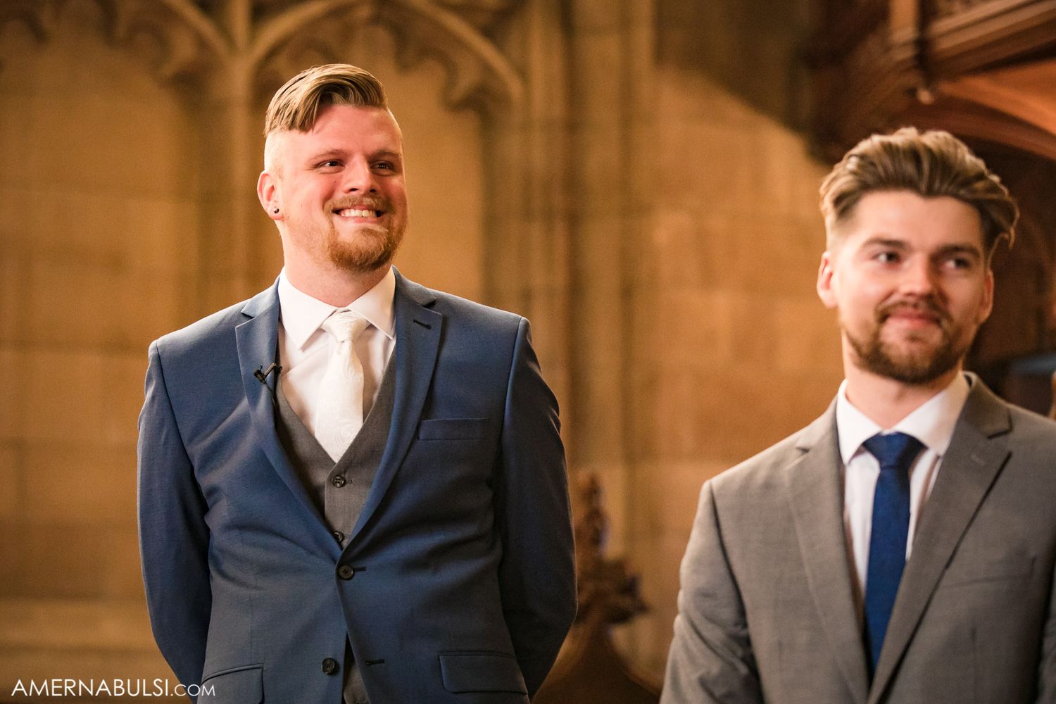 Two groomsmen standing in gothic church interior with stone archways.