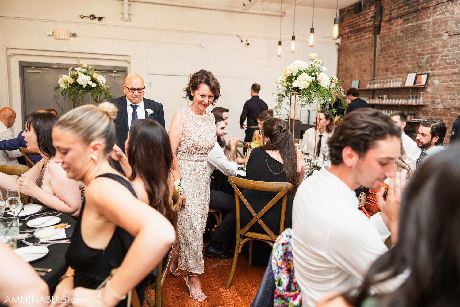 Wedding reception guests enjoying dinner in an industrial-chic venue with brick walls.