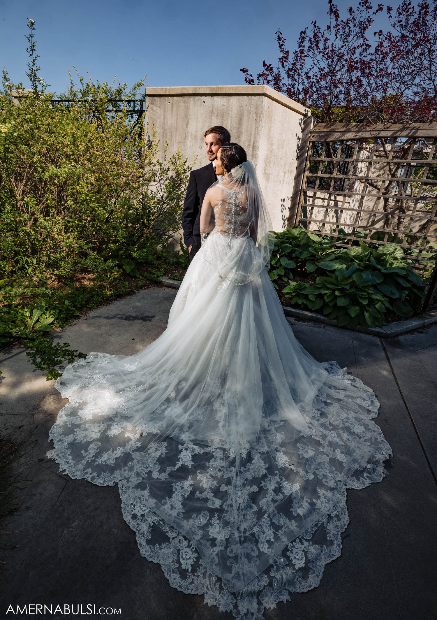 Stunning bridal portrait showcasing intricate lace train of wedding gown against garden setting.
