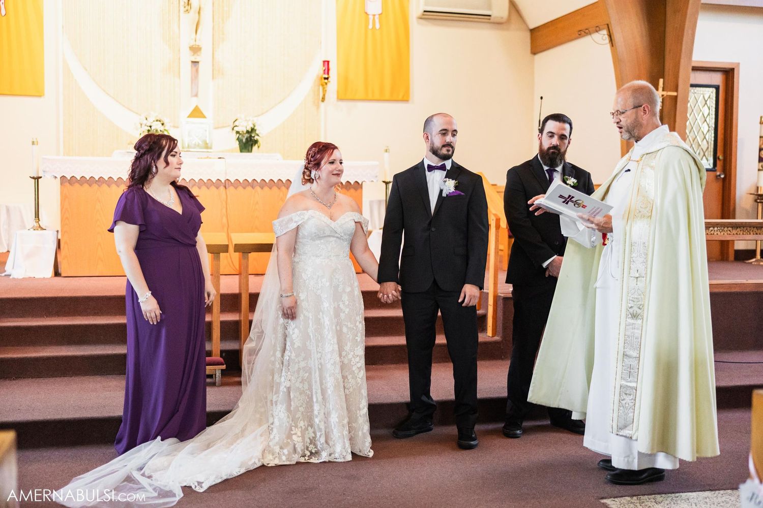 Wedding party standing at church altar with priest during ceremony.