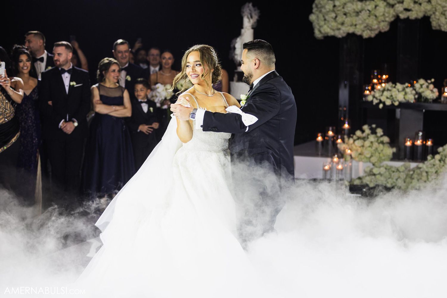 Couple shares romantic first dance on misty dance floor with floral decor.