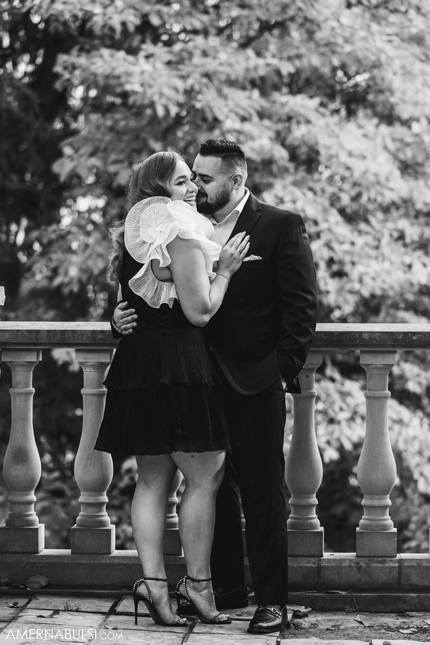 Romantic couple embracing on stone balcony during outdoor photo session.