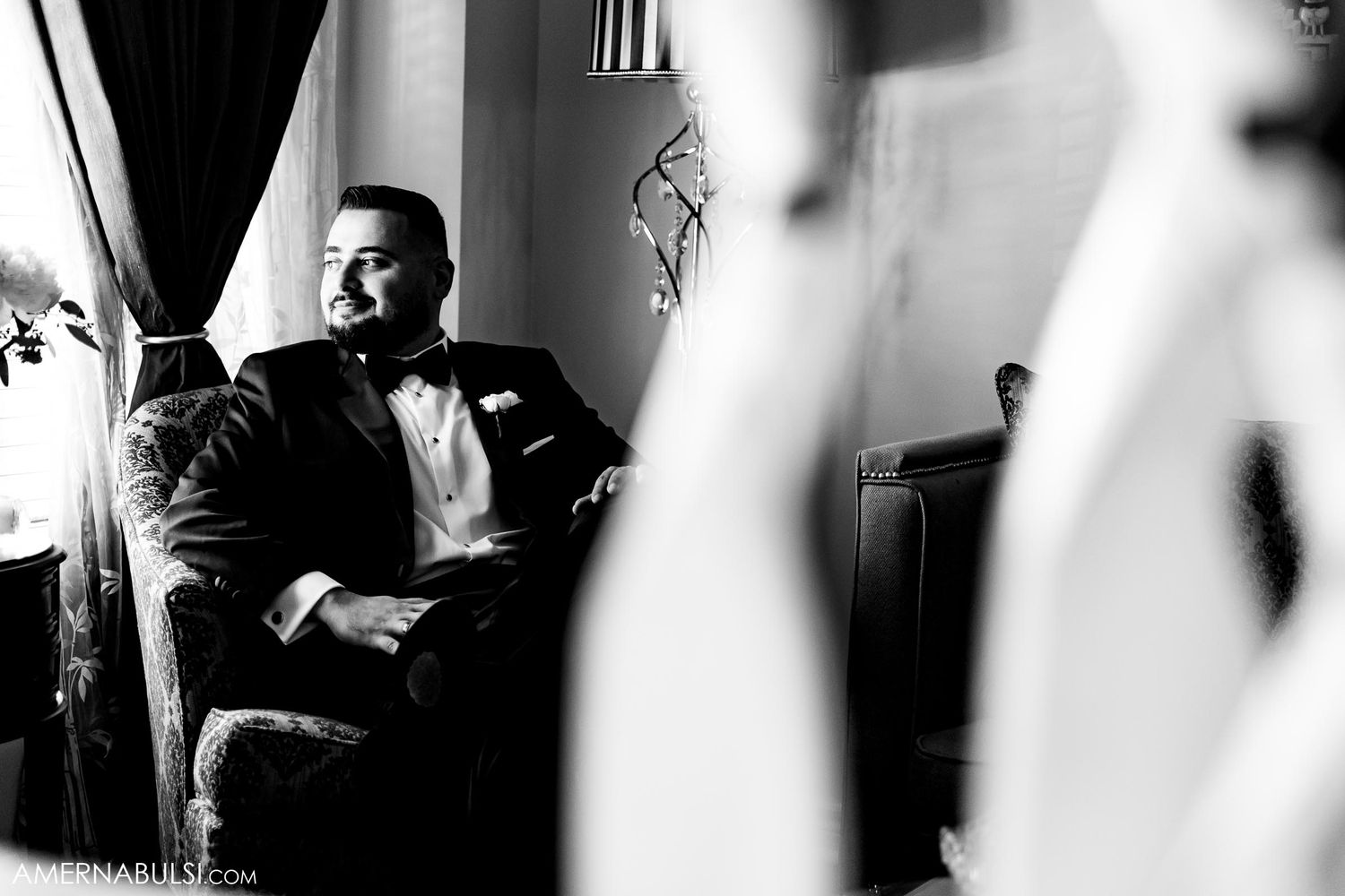 Artistic black and white portrait of a person in formal attire seated by window light.