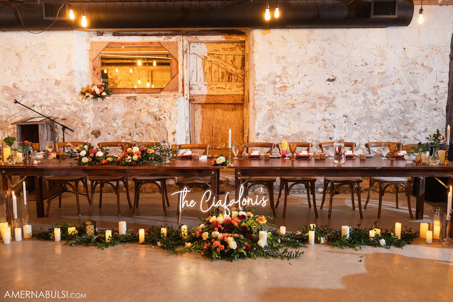 Rustic wedding reception table setup with candlelight and floral centerpieces.