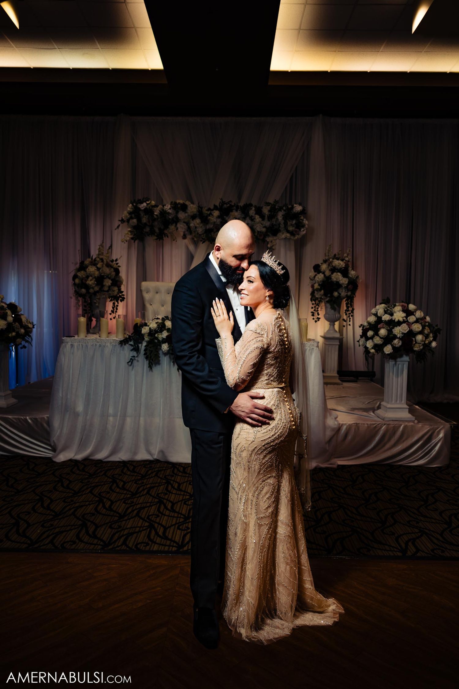 Romantic ballroom wedding dance with floral arrangements and draped fabric backdrop.