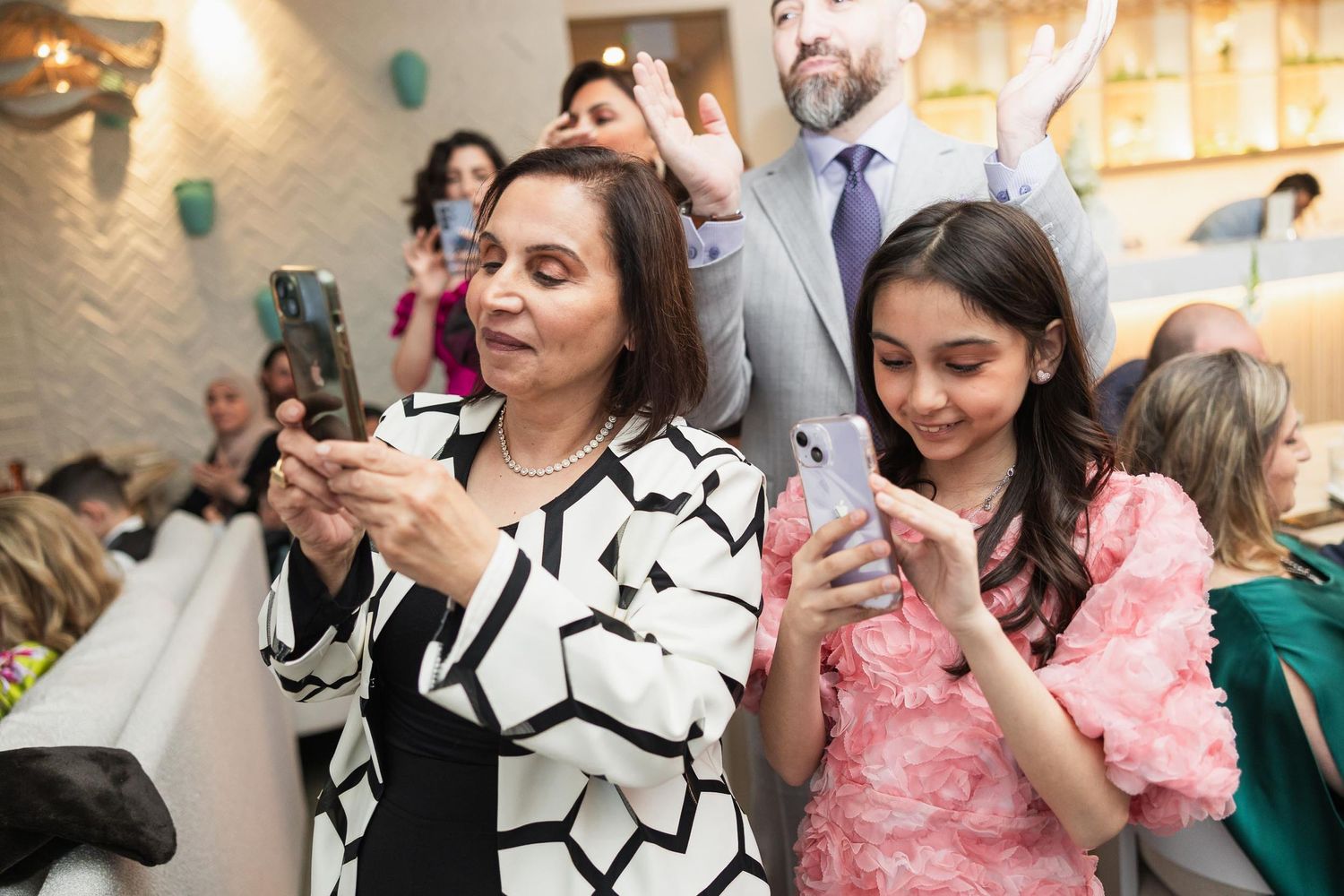 Wedding guests celebrate enthusiastically with phones raised during a reception party moment.