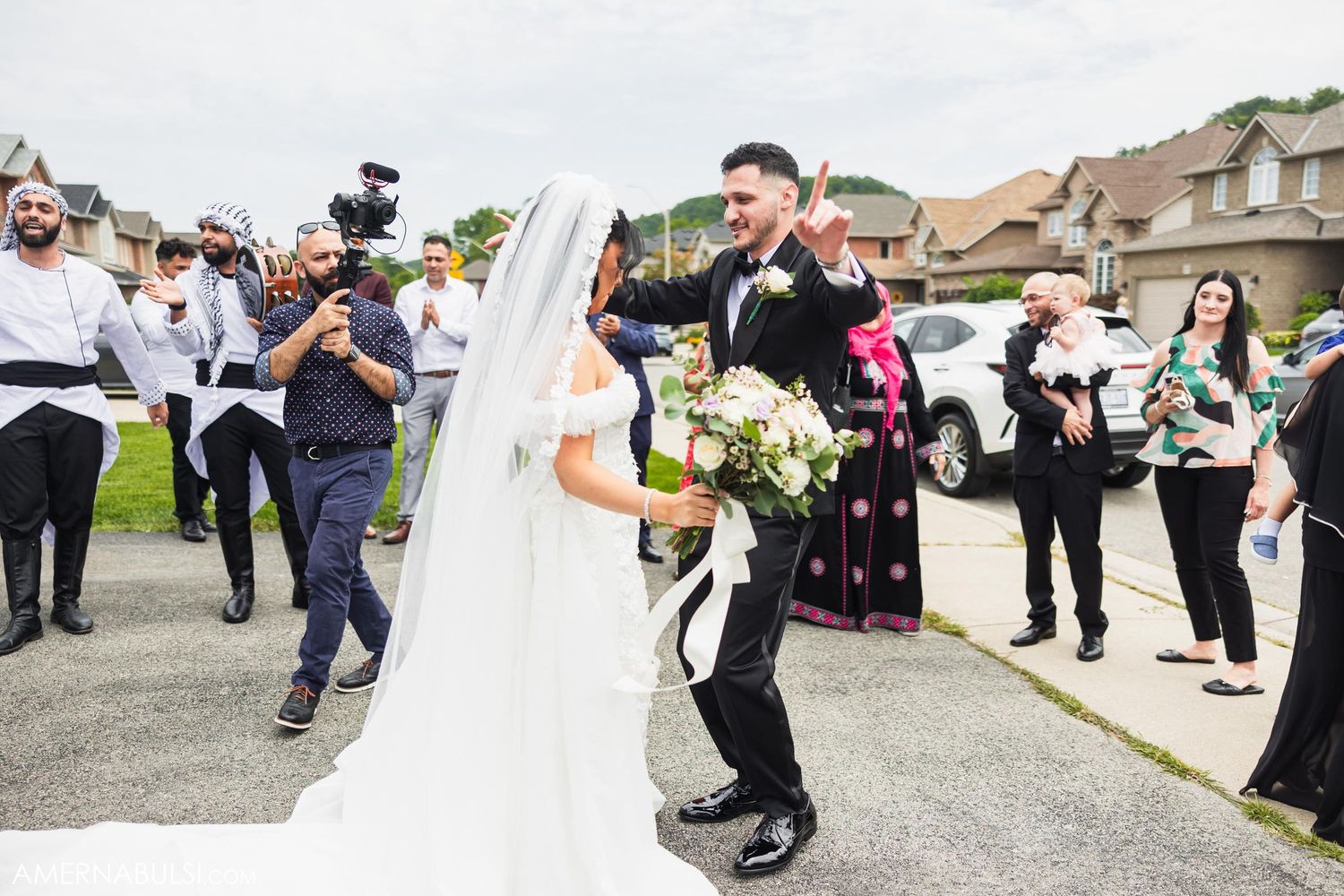 Wedding photographer captures couple during outdoor celebration among cheering guests.
