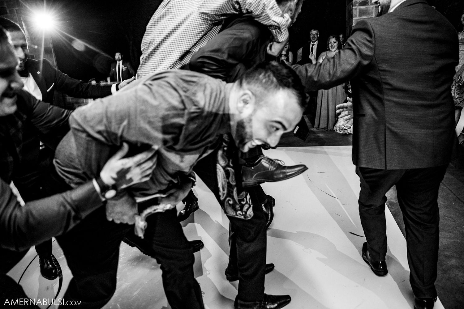 Black and white photo of wedding guests dancing with dramatic lighting and shadows on the dance floor.