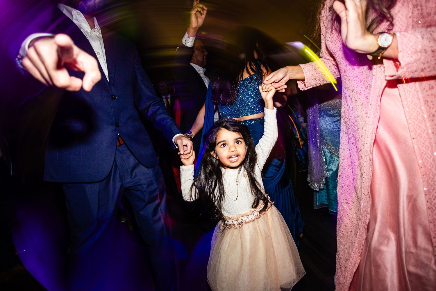 Wedding guests dancing and celebrating on a dark dance floor with purple lighting and pink accents.