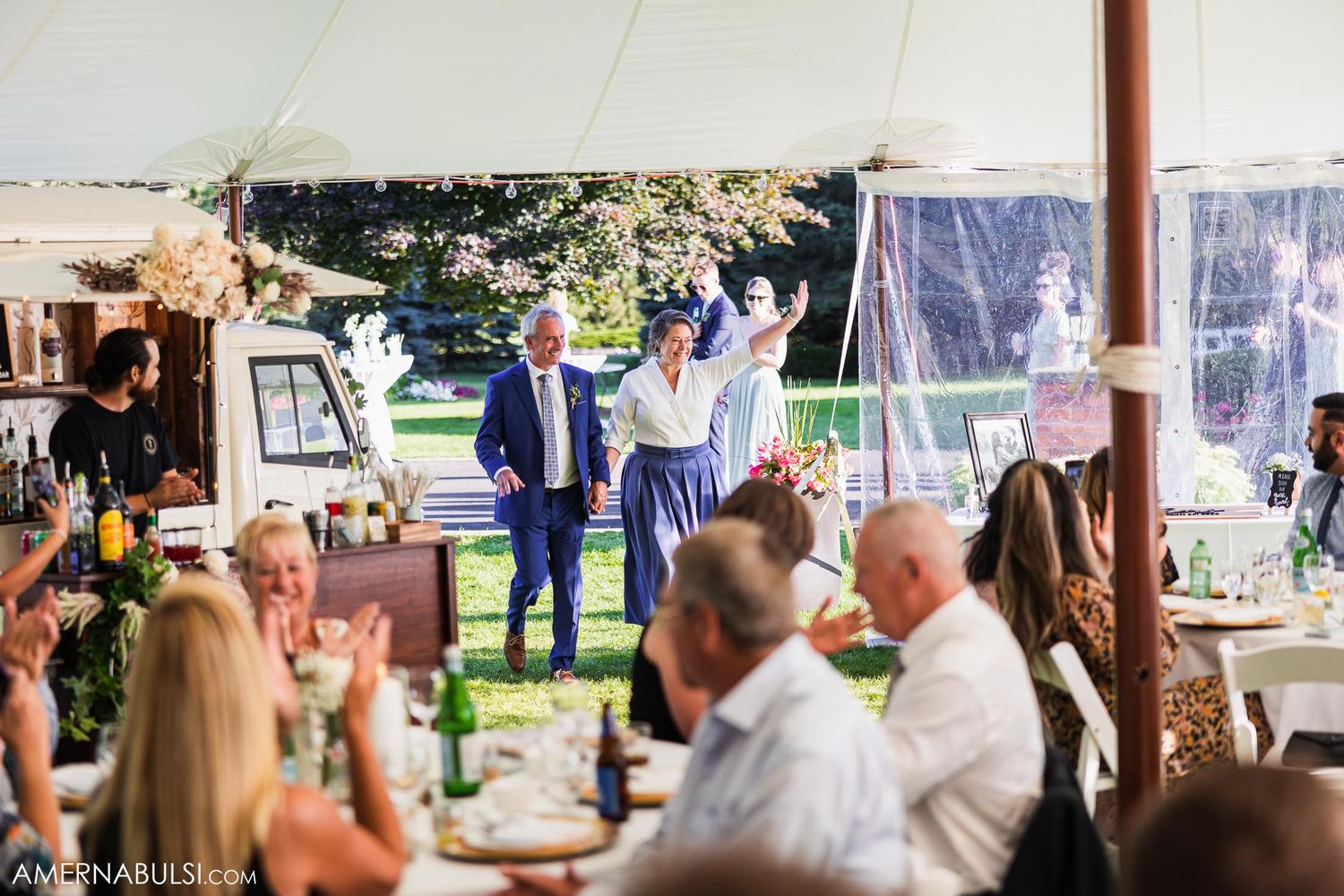 Wedding celebration under tent with guests seated at tables while others celebrate.