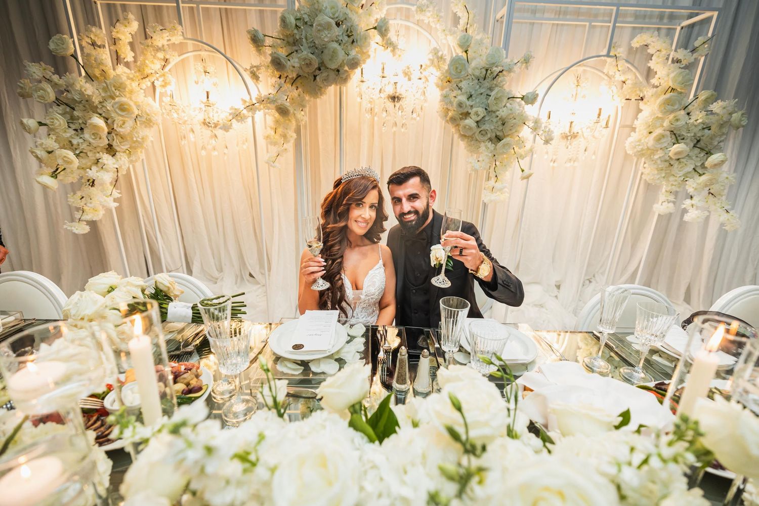 Newlyweds celebrate at their elegant reception with white floral decorations and crystal chandeliers.