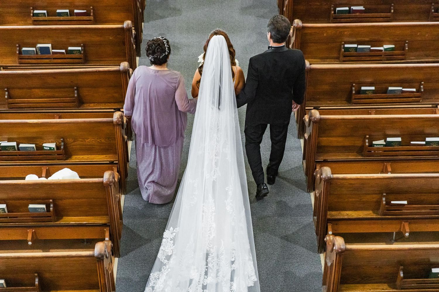 A bride in white gown walks down the church aisle accompanied by wedding party members.