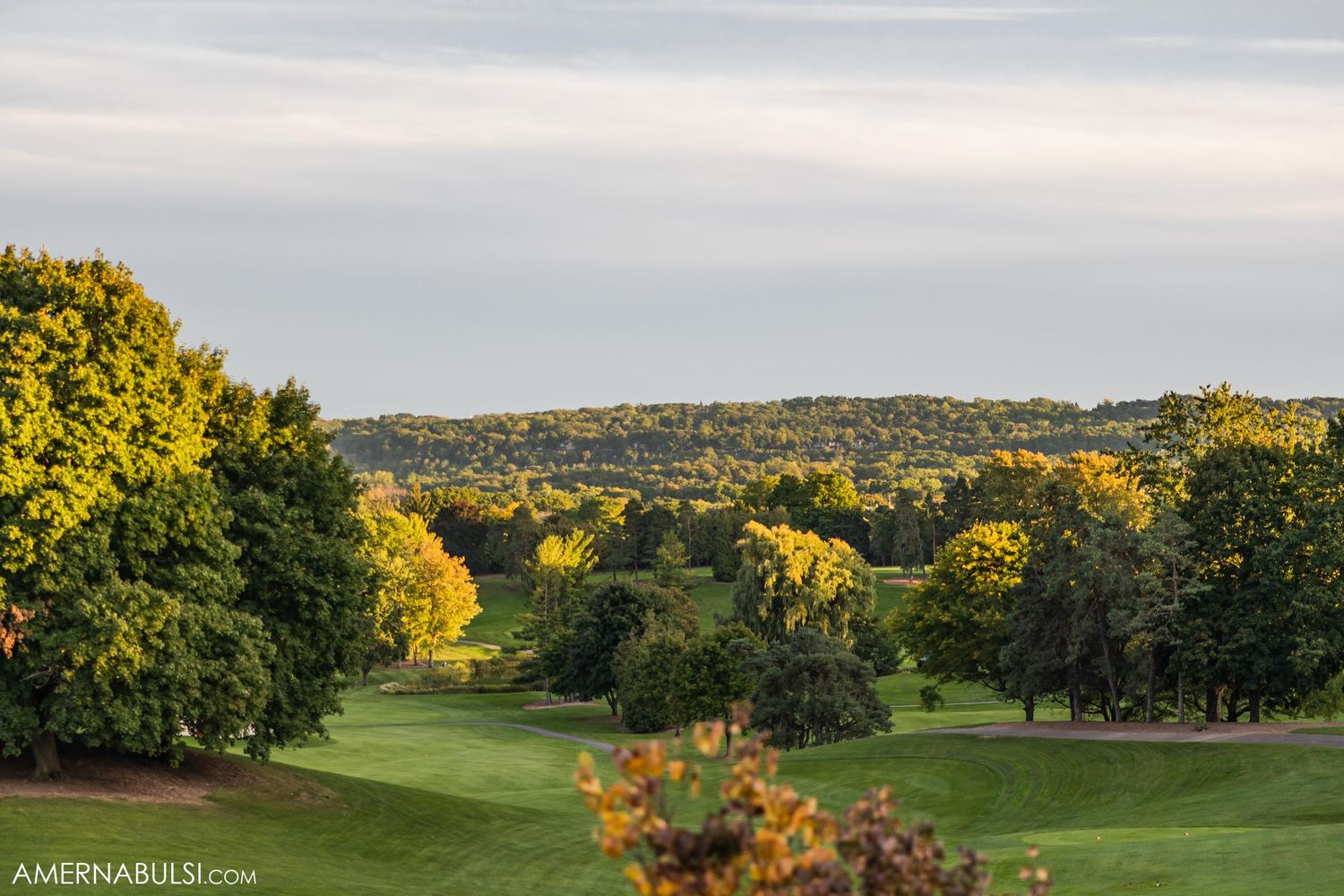 Scenic view of rolling hills and autumn trees on golf course at sunset.