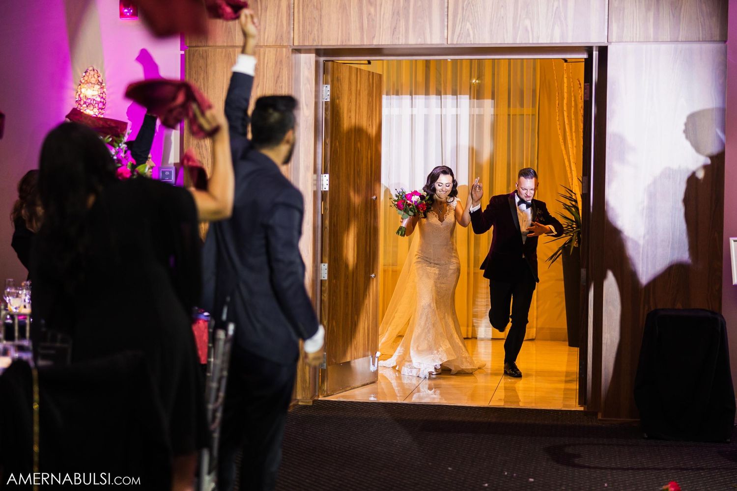 Grand entrance of wedding couple through doorway with dramatic backlighting and silhouetted guests.