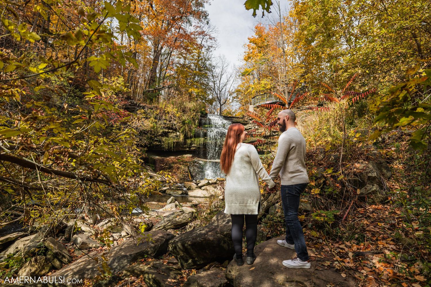 Couple walking on rocky path with autumn waterfall in background.