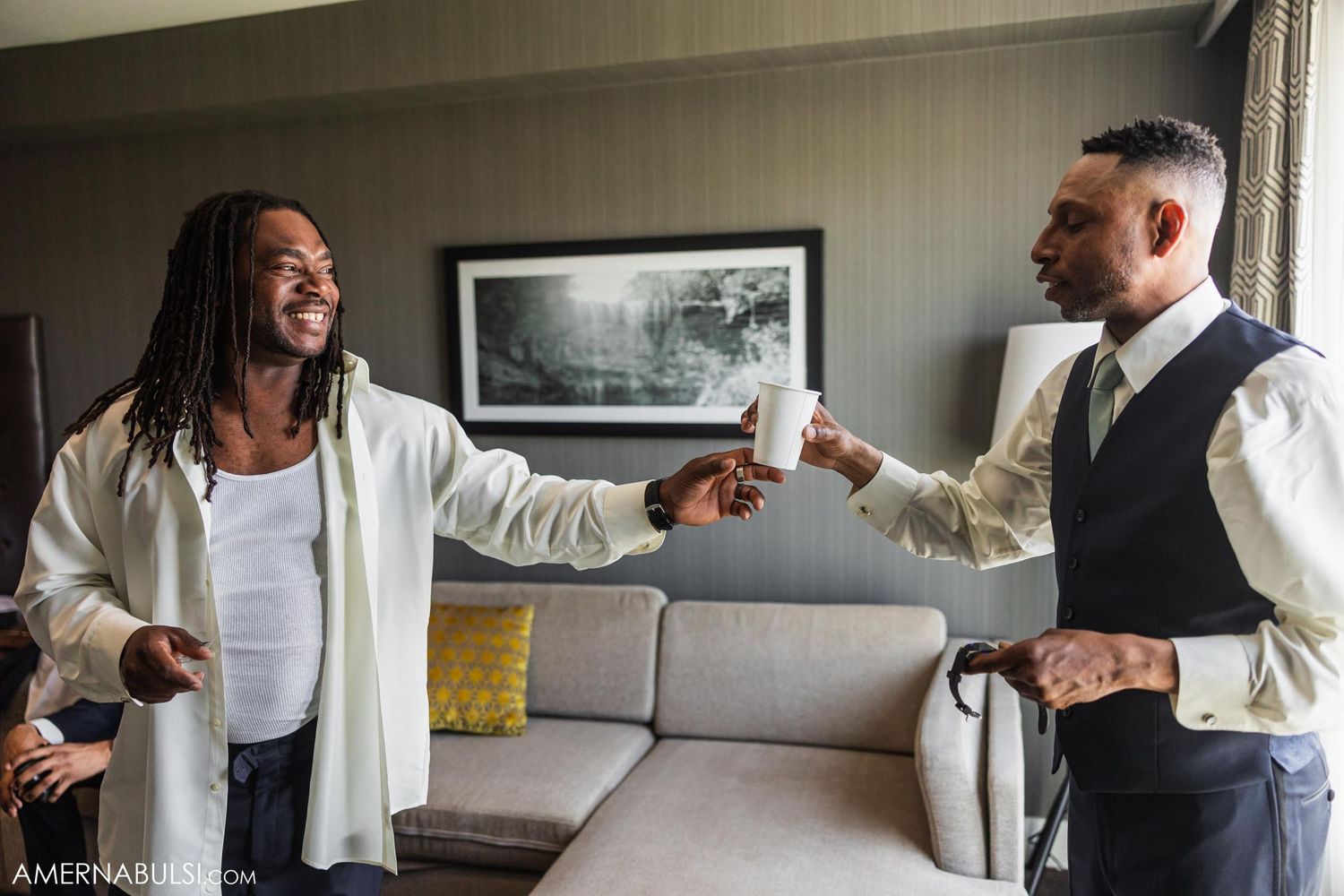 Two people share a joyful moment while getting ready, one in a white shirt and one in a vest.