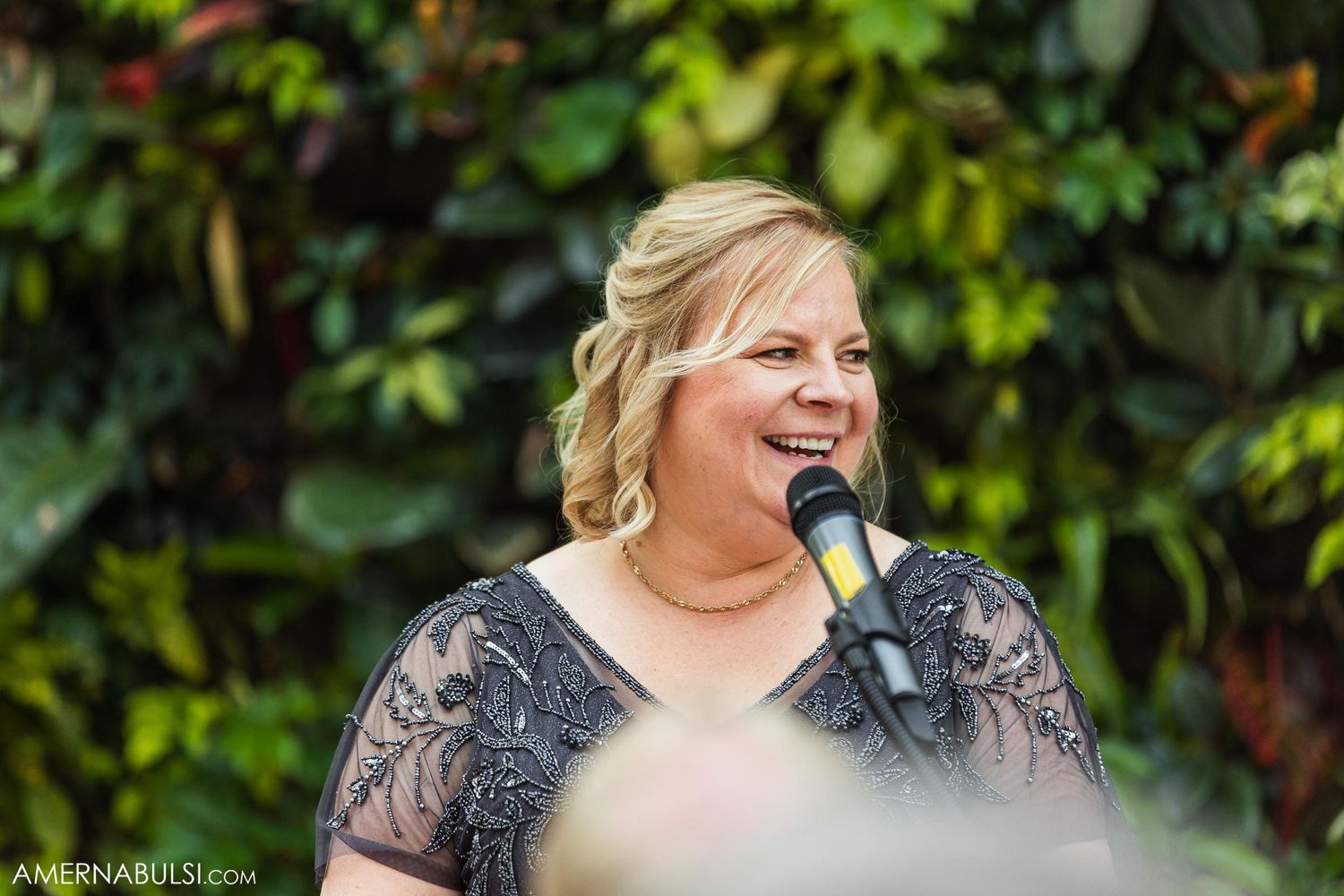 A person in lace speaks with joy at an outdoor wedding celebration.
