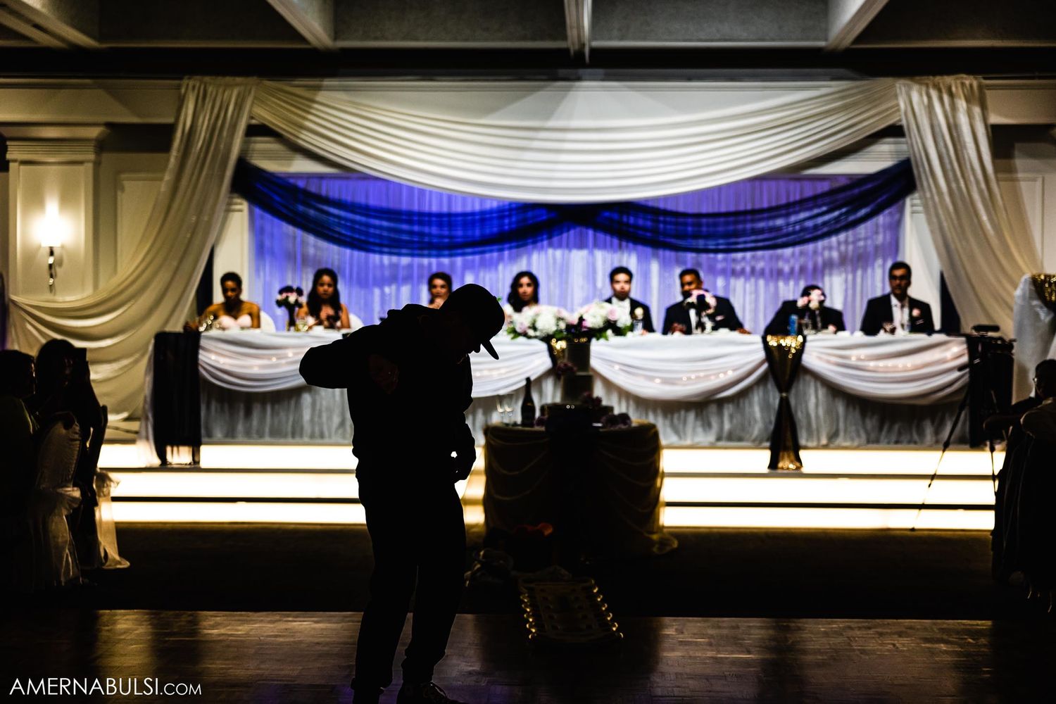 Silhouette of wedding party members at head table with blue backdrop lighting.