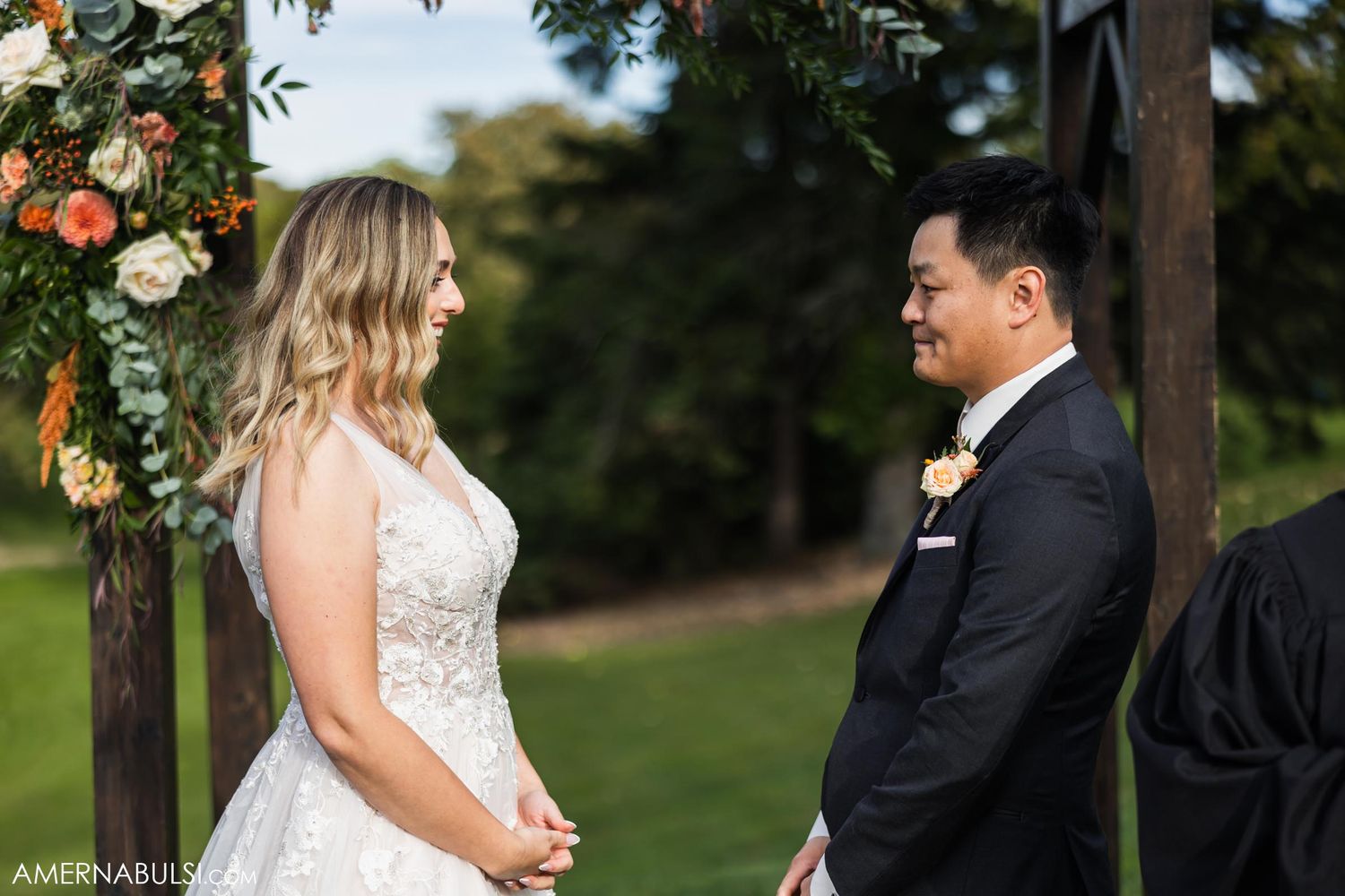 A couple exchanges intimate glances during their outdoor wedding ceremony beneath floral decor.
