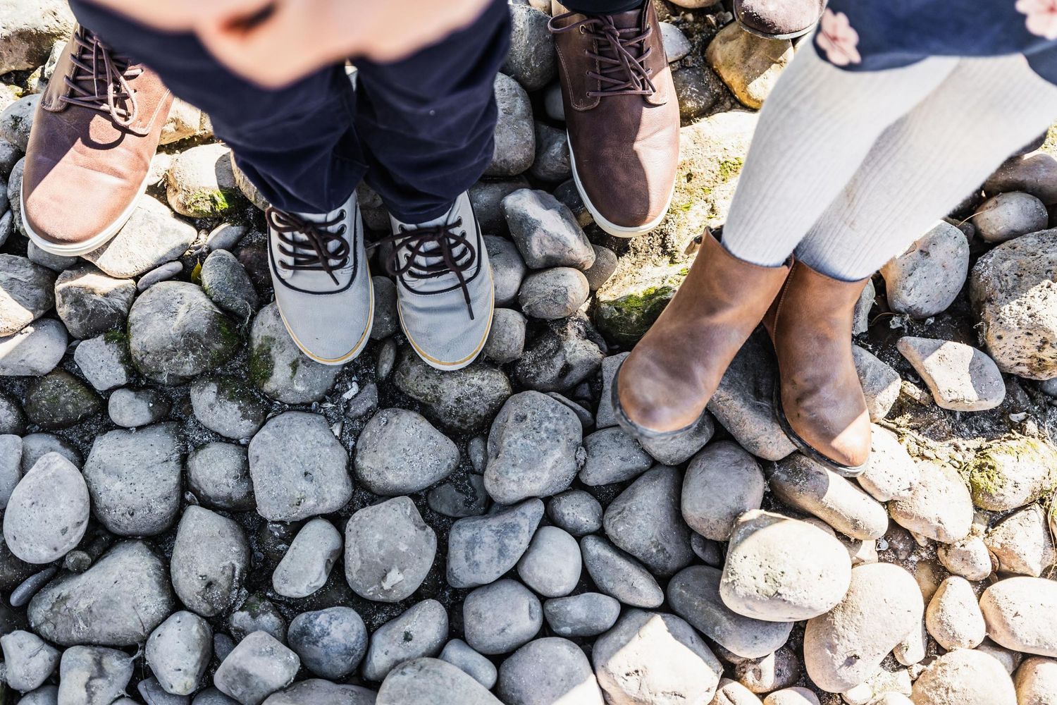 Shoes of a couple standing on smooth river rocks by the water.