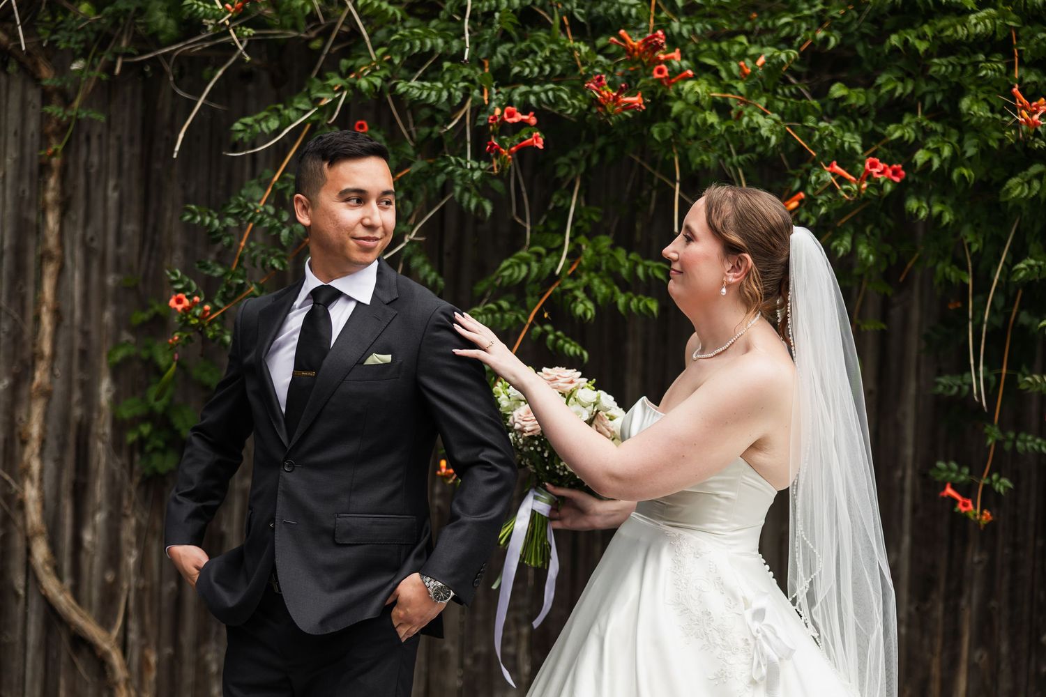 Bride in white lace gown with veil holds bouquet as groom in dark suit turns during first look.