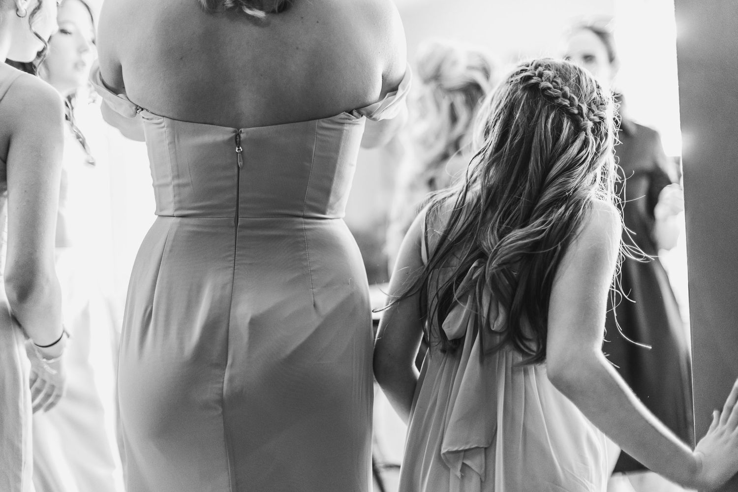 Black and white photo of bridesmaids and flower girl with braided hair standing together during wedding preparations.
