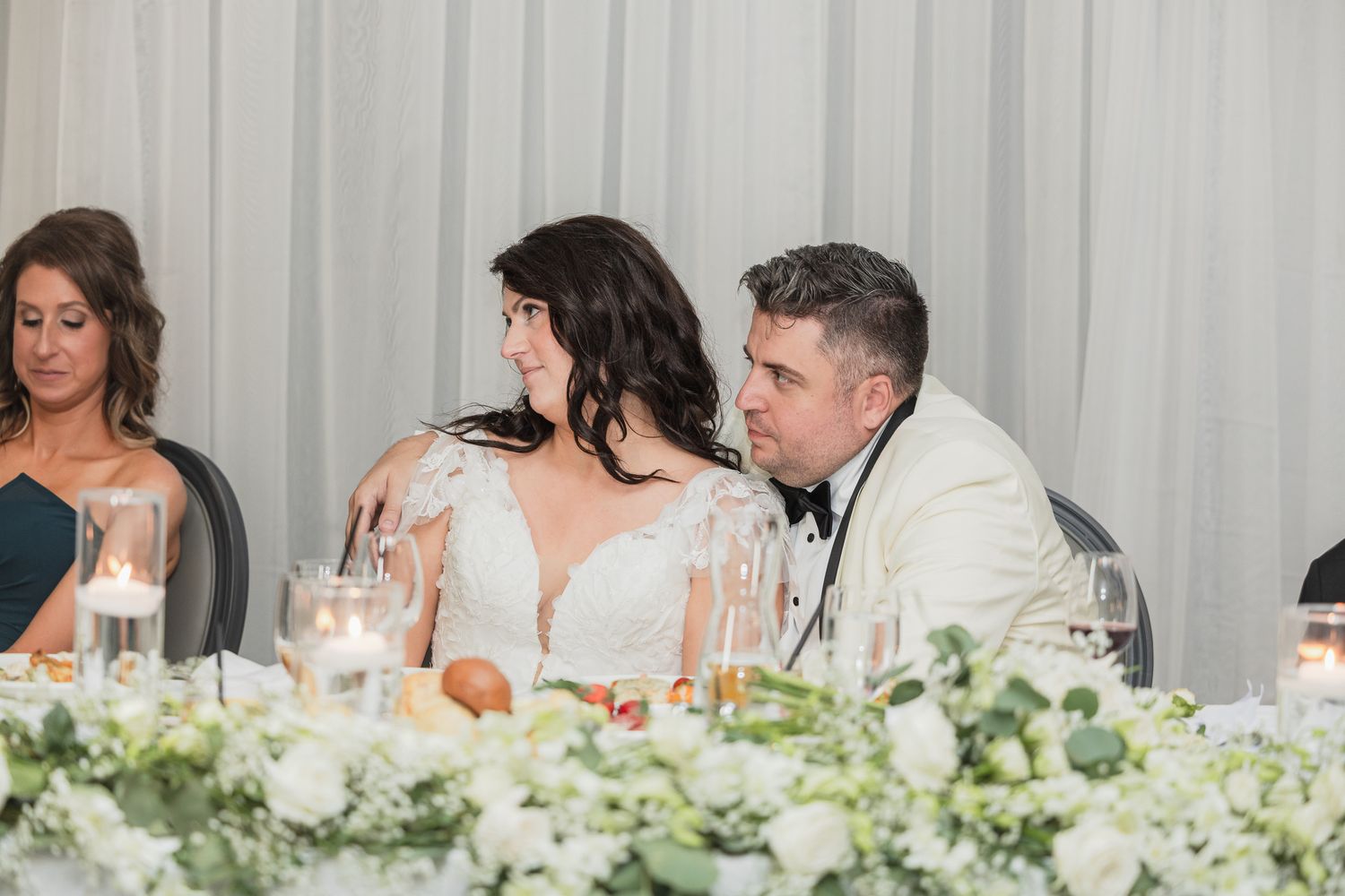 Bride and groom share an intimate moment at the wedding reception head table surrounded by floral arrangements.