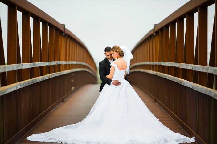 Wedding couple embraces on a wooden bridge walkway surrounded by natural scenery.