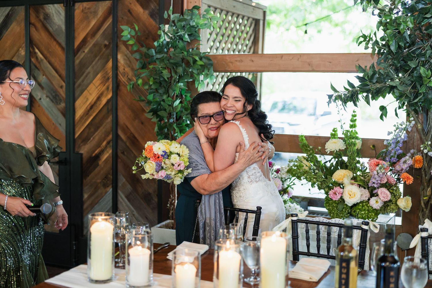 Bride and groom share a joyful hug at their wedding reception table adorned with candles and floral arrangements.