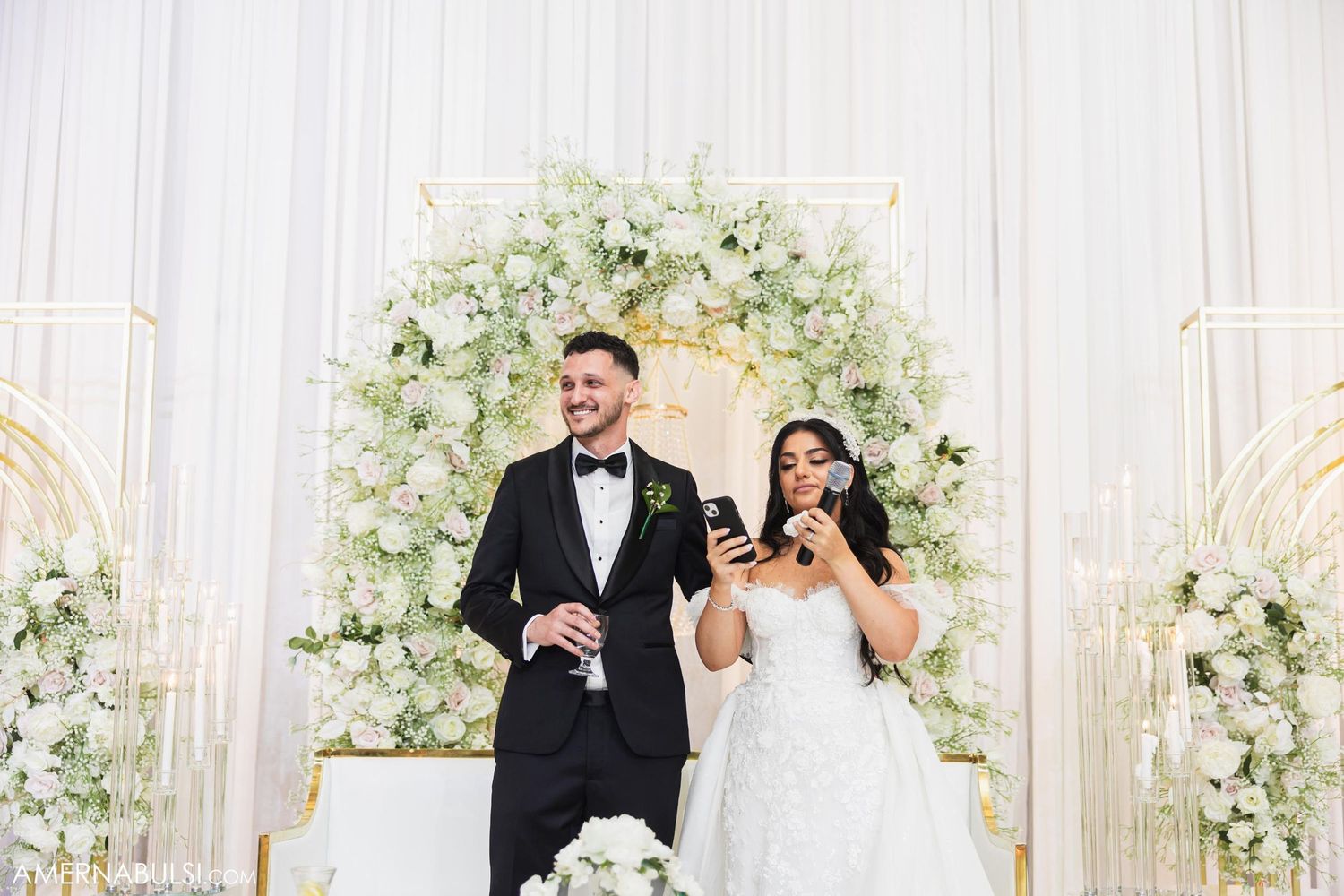 Newlyweds celebrate under a luxurious white floral arch at their wedding ceremony.