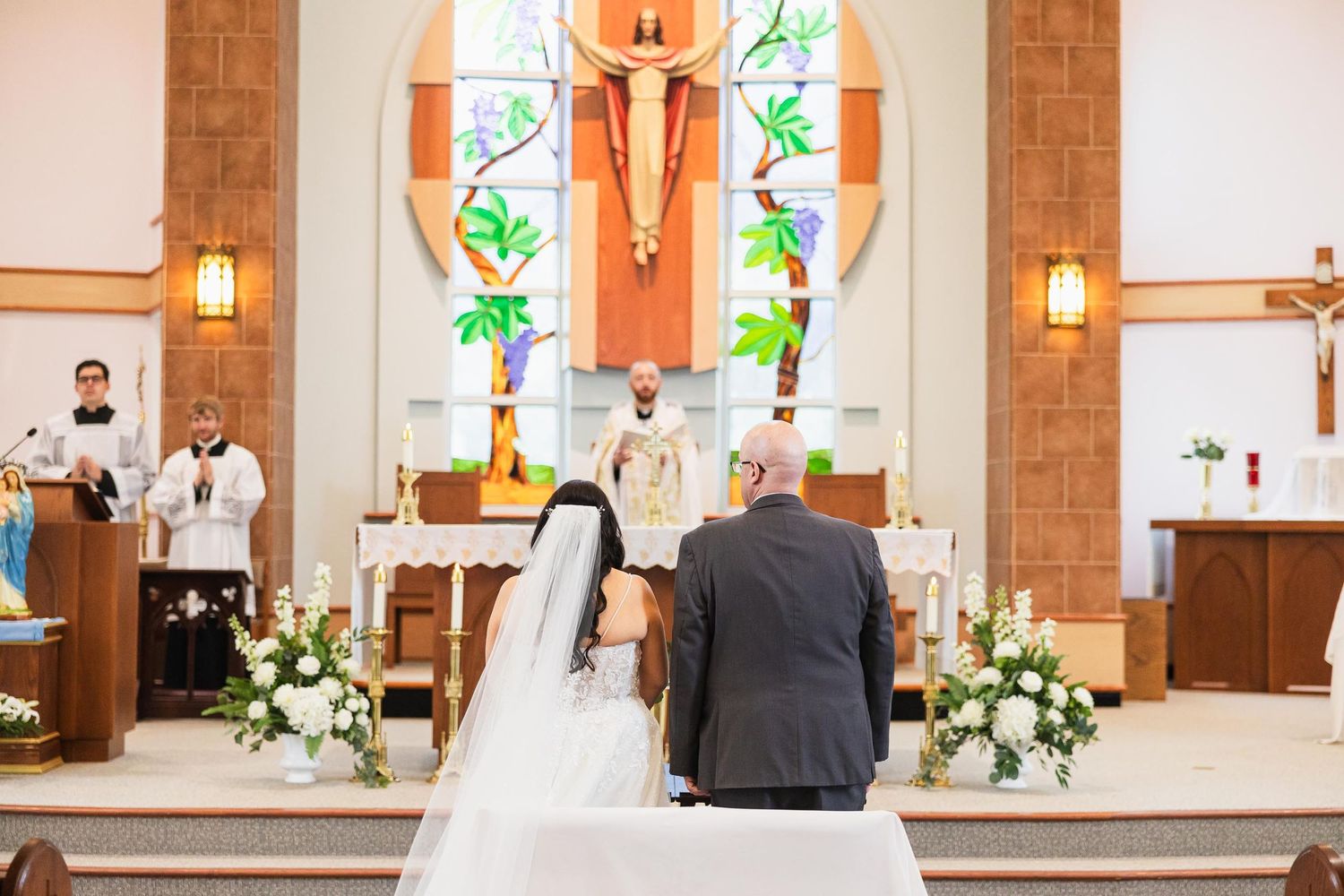 Ceremony at church altar decorated with white flowers and stained glass windows.